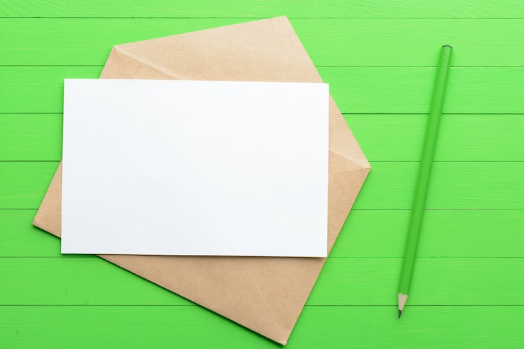Photo a blank piece of paper with an envelope on green wooden background