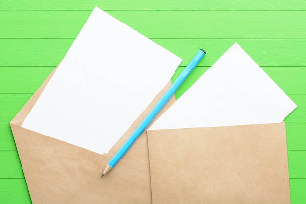 Чистый лист бумаги с конвертом на зеленом деревянном фоне