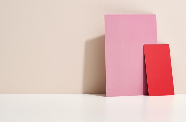 Blank pink and red cardboard sheet of paper with shadow on white table Template for flyer announcement