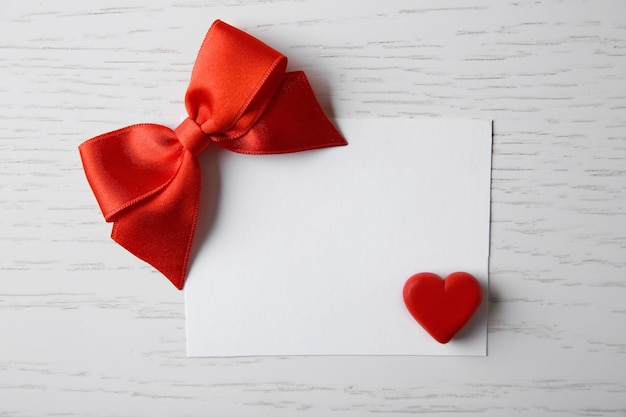 Blank present card with ribbon bow and small heart on wooden background