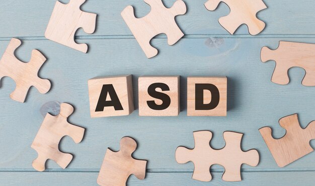 Puzzle vuoti e cubi di legno con il testo asd autism spectrum disorder si trovano su uno sfondo azzurro.