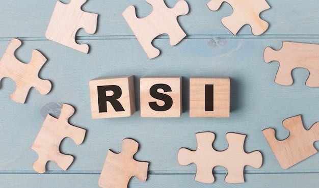 RSI 상대 강도 지수(RSI Relative Strength Index)라는 텍스트가 있는 빈 퍼즐과 나무 큐브는 밝은 파란색 배경에 있습니다.