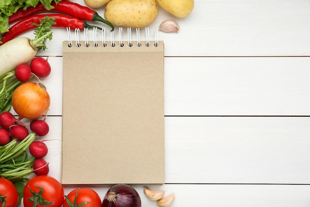 Blank recipe book and different ingredients on white wooden table flat lay Space for text