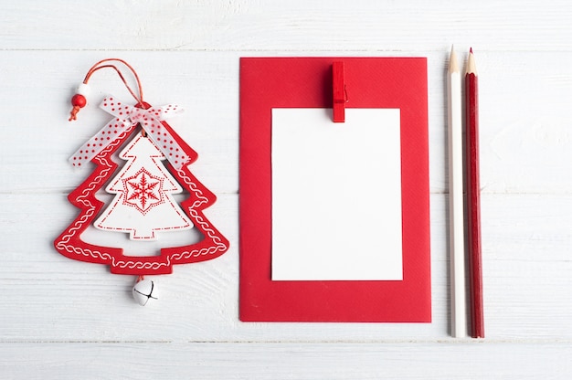 Фото Пустой красный конверт, пустая записка и белые рождественские игрушки на деревянном деревенском плоском основании