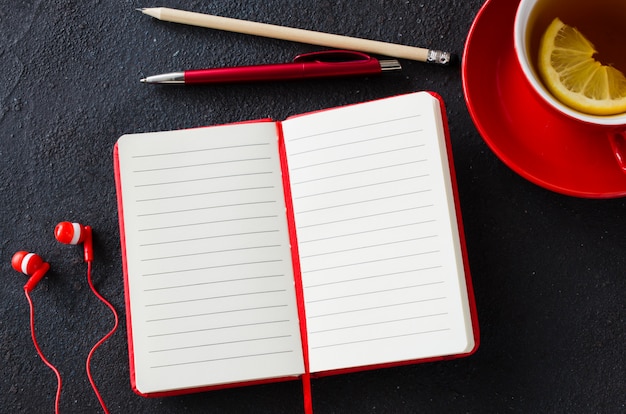 Blank red notebook, computer laptop, headphones and cup of tea. Business or education concept.