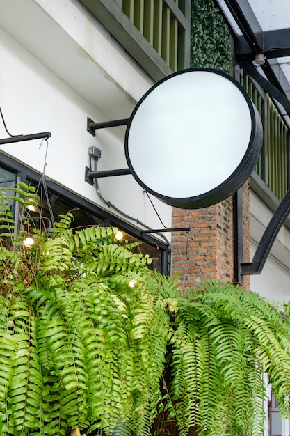 Blank round shop sign light box hanging on retro cafe with plant leaves