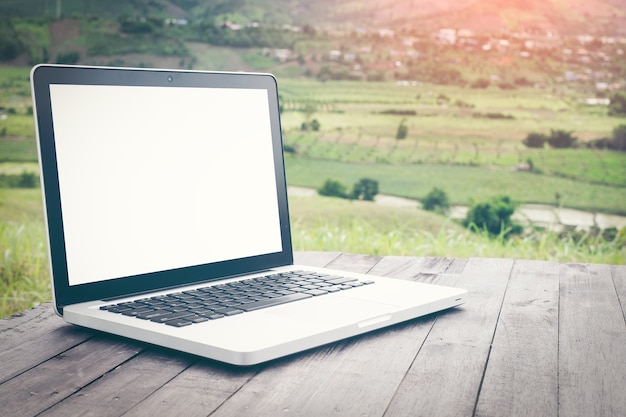 Computer portatile dello schermo in bianco sulla natura pittoresca del fondo, ufficio all'aperto.