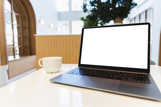 L'uomo moderno del computer portatile dello schermo vuoto usa il computer portatile della stanza con lo schermo desktop bianco vuoto con la tazza di caffè sulla tavola di legno in caffè