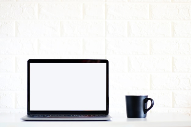 空白の画面ノートパソコンと白いレンガの壁の背景に黒いコーヒーのカップ