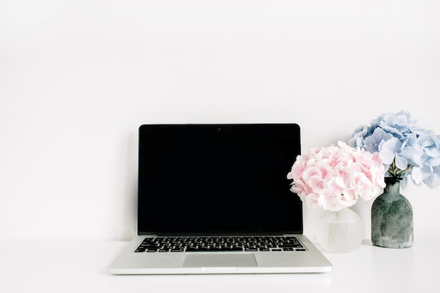 Blank screen laptop and pink and blue hydrangea flower bouquets on white surface