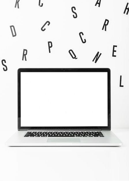 Blank screen laptop with scattered alphabets on white background