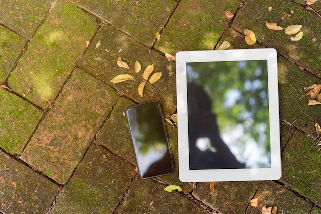 Пустой экран мобильного телефона и планшета на полу в саду