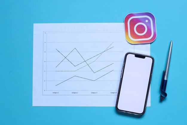 A blank screen of smartphone and pen with graph paper and Instagram logo icon. Instagram growth tren