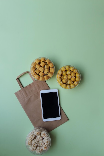 갈색 종이 봉지에 빈 화면 태블릿과 밝은 녹색 배경 온라인 비즈니스 개념이 있는 다양한 쿠키 항아리
