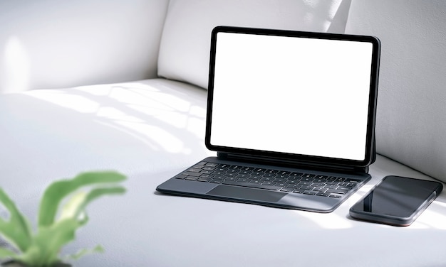 Blank screen tablet with keyboard and smartphone on white leather couch in living room.