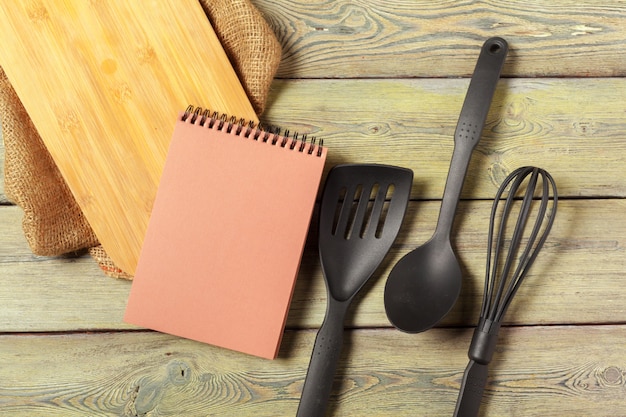 Blank sheet of opened notepad and kitchen utensils on  table with tablecloth, copy space