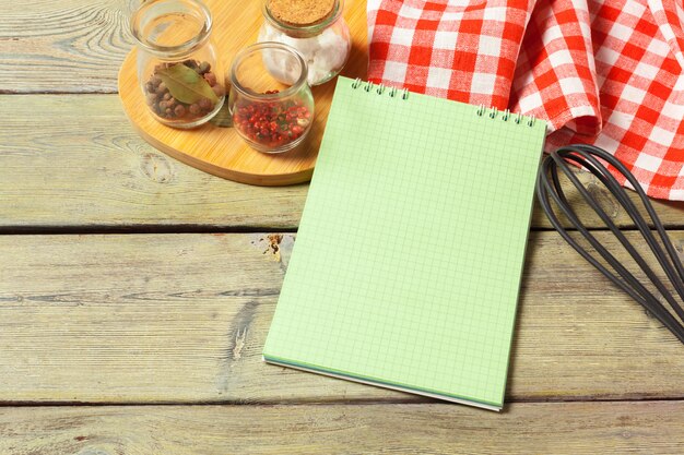 Blank sheet of opened notepad and kitchen utensils on  table with tablecloth, copy space