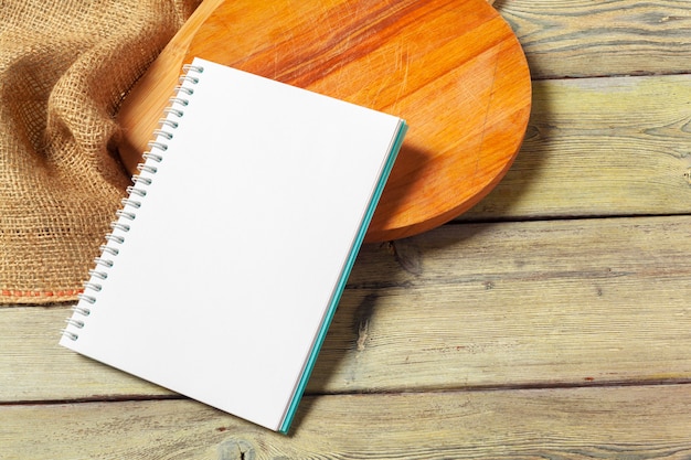 Blank sheet of opened notepad and kitchen utensils on  table with tablecloth, copy space