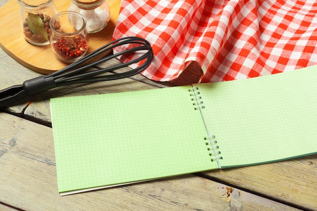 Blank sheet of opened notepad and kitchen utensils on  table with tablecloth