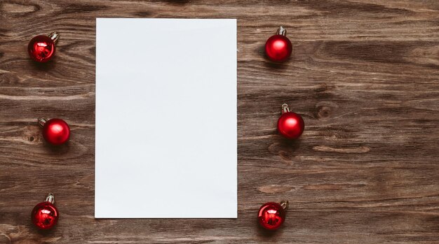 A blank sheet of paper and and red Christmas balls on a wooden background Top view flat lay