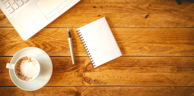 A blank sheet of paper with pen on a wooden work table with a coffee cup.