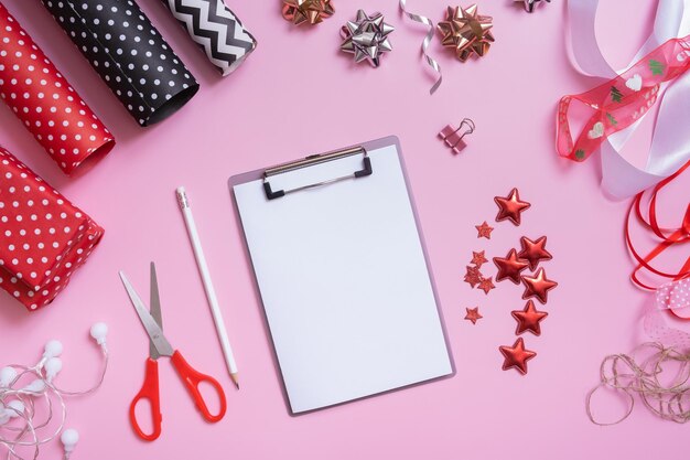 Blank sheet of paper and wrapping materials for christmas presents flat lay on pink background