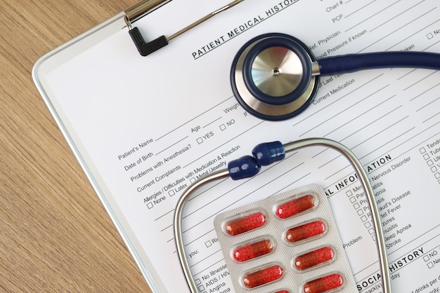 Photo blank sheet of patients medical history form with stethoscope and pills top view medical