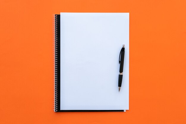 Blank sheet with notebook and pen on orange background.