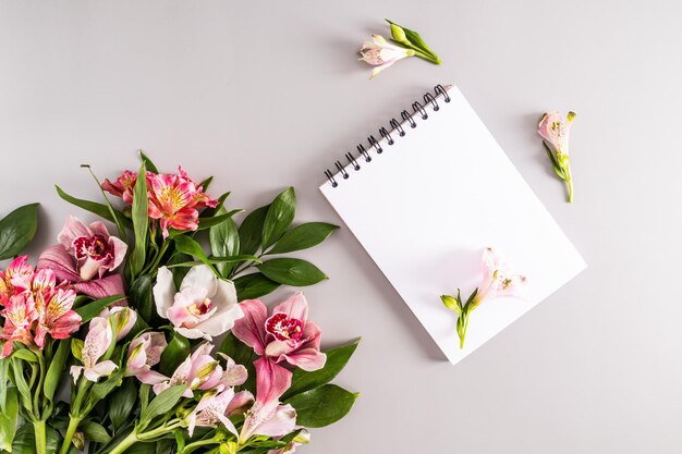 Blank sheets of notebook on a black spring and a bouquet of spring flowers on a pastel background top view festive background