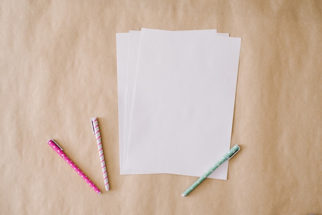 Blank sheets of white paper and colorful pens on a crafting paper