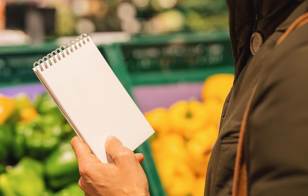 Blank Shopping list in the hand of a woman in a supermarket with copyspace for your individual text