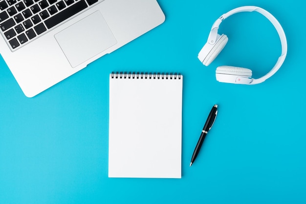 Photo blank spiral notepad on turquoise background with laptop headphones and fountain pen