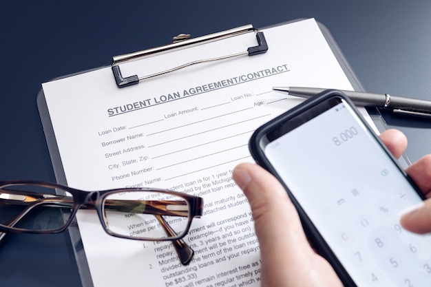 Blank Student Loan Application with phone calculator, pen and glasses on table on black background