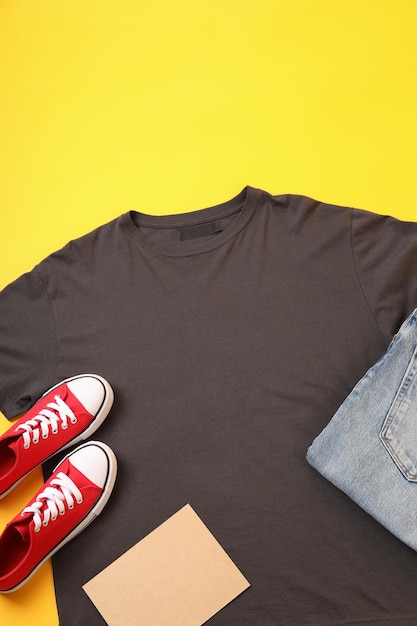 Blank t-shirt, jeans, sneakers and carton sheet on yellow background