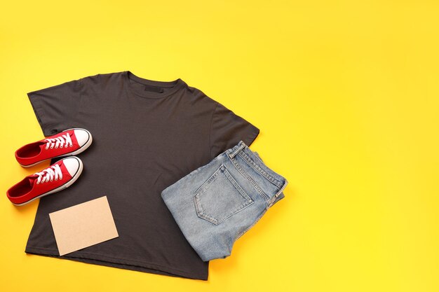 Blank t-shirt, jeans, sneakers and carton sheet on yellow background