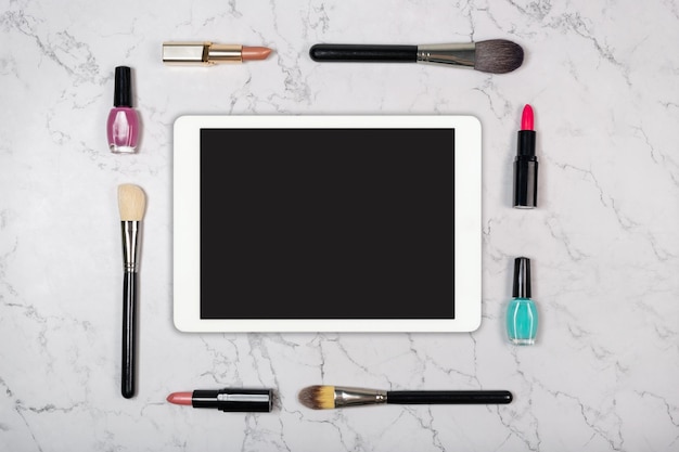 Blank touchpad with makeup brushes and cosmetic products on natural white marble texture tablet comp