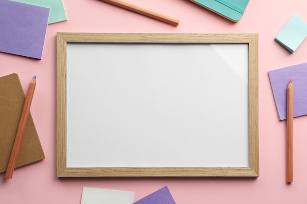 Blank white board with stationery on light pink background flat lay Space for text