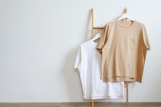 木製の服架に展示されたハンガーに白と茶色のTシャツのモックアップ