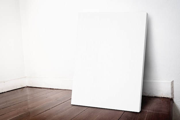 Foto telaio di tela bianca vuota che si appoggia al muro di casa grunge e pavimento in parquet marrone scuro
