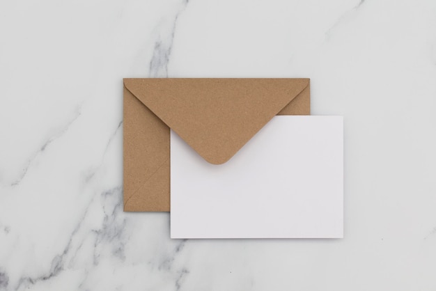 Carta bianca vuota con busta di carta marrone kraft su sfondo di marmo