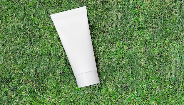 Blank white cosmetic tube mockup the green lawn covered with grass Top view