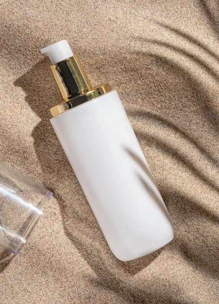 ベージュの砂の上から見たヤシの葉のハードシャドウ化粧品のモックアップに空白の白いクリームボトル