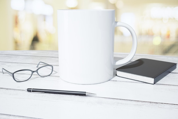 Blank white cup with diary pen and eyeglasses on white wooden table