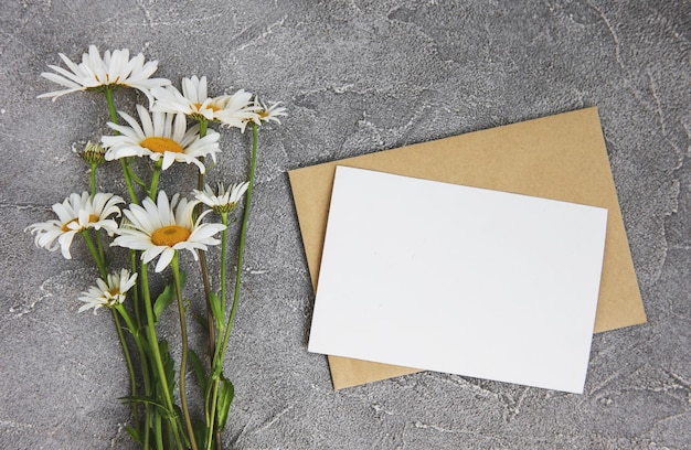 blank white greeting card and envelope with chamomile flowers on a gray stone background