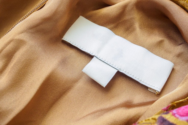 茶色の布のテクスチャ背景に空白の白い洗濯ケア服のラベル
