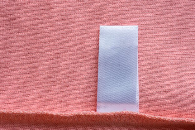 Blank white laundry care clothes label on pink fabric texture background