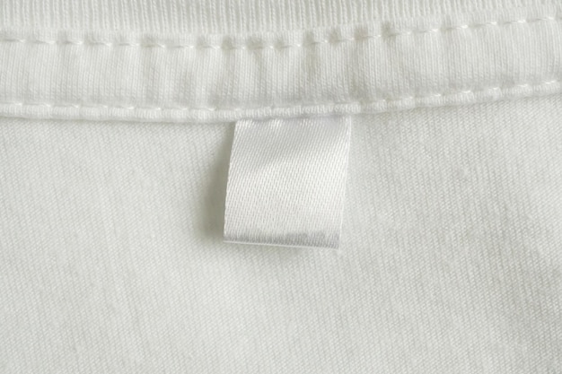 Photo blank white laundry care clothes label on white shirt fabric texture background