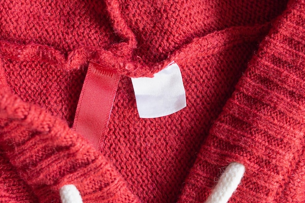 Blank white laundry care clothing label on red knitted texture background