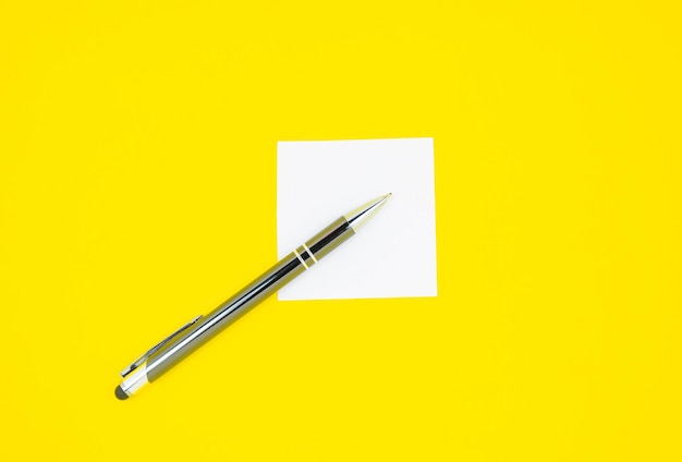 Photo blank white to do list sticker with pen. searching information on the internet.
close up of reminder note paper on the yellow background. copy space. minimalism, original and creative.