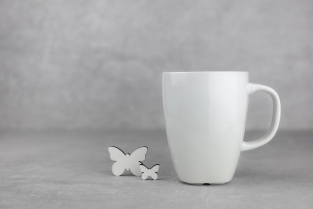 Foto mockup di tazza bianca vuota con farfalla bianca su superficie di pietra di cemento grigio chiaro